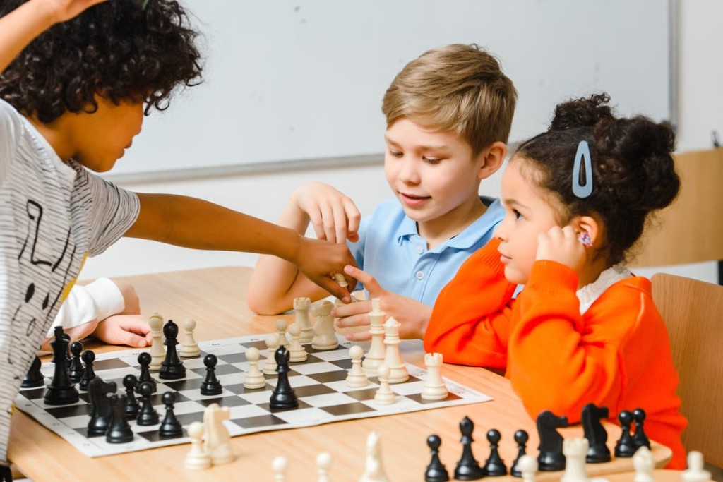 Three children focused on a chess game in a bright classroom